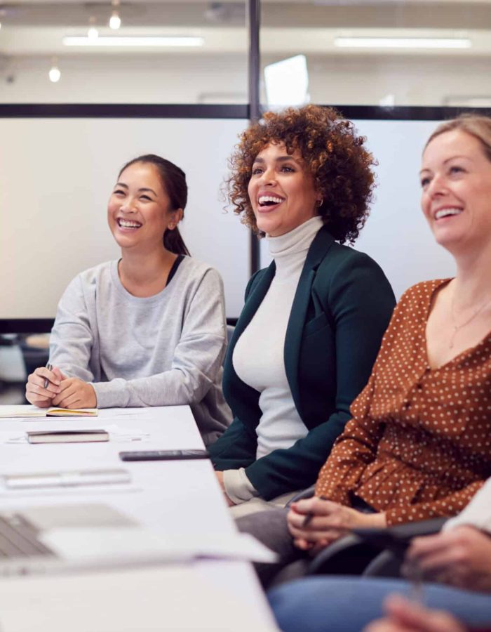 Line Of Businesswomen In Modern Office Listening To Presentation By Colleague